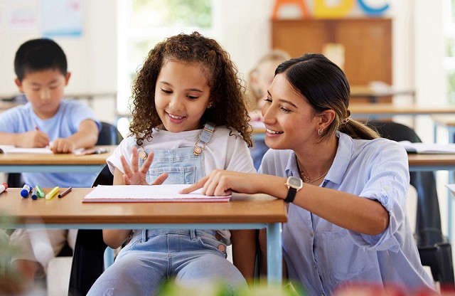 A pupil holding a pencil and looking at a teacher